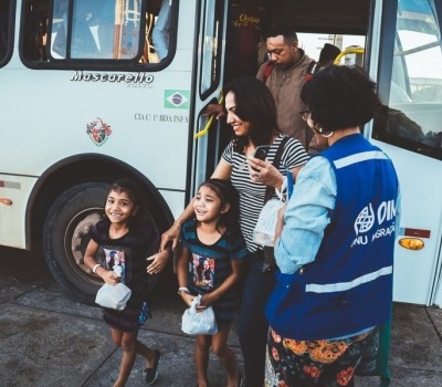 Children and their families arrive on a bus looking excited in IOM Brazil